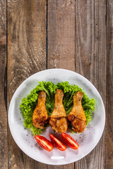 Fried chicken drumsticks with vegetables on wooden table