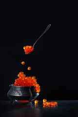 Spoon with red caviar on a black background. Vintage vase on the table. Gourmet Concept.Copy space.