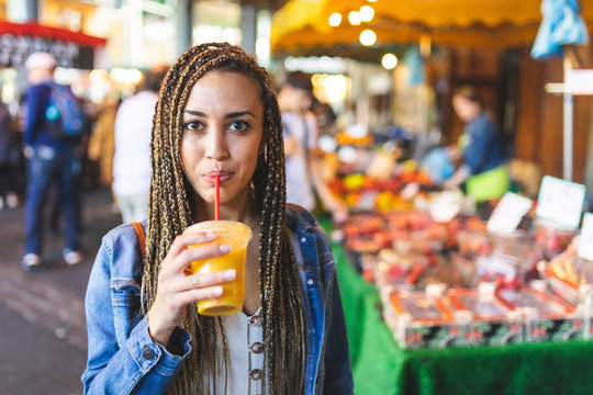 Portrait Of Young Woman Drinking Fresh Orange Juice On Street Market, London, UK