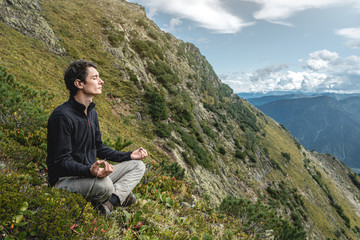 Man hiker sitting in a yoga pose at the peak of the mountain in the summer. Meditation after a long climb on a mountain