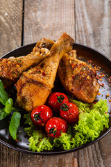Fried chicken drumsticks with vegetables on wooden table