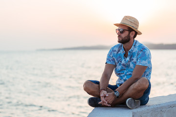 Fototapeta na wymiar Young bearded man sitting by the sea in sunset