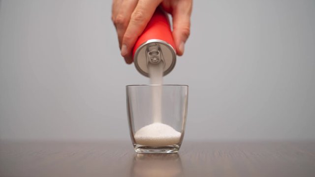 Close-up demonstration video of a man filling glass with sugar from red soda can. Sugar in soft drinks and sodas. Isolated, on white background