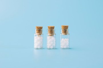 Homeopathic globules and glass bottle on blue background. Alternative Homeopathy medicine herbs, healtcare and pills.