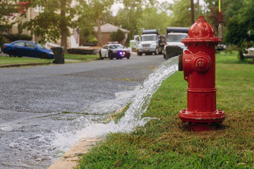 Water flowing from an open red fire hydrant is wet from the spray.