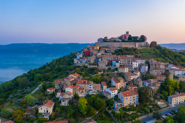 Obraz premium The ancient city of Motovun is located on the top of the mountain. The city is surrounded by a fortress wall. The background image are mountains and fog at the foot of the mountains. Istria, Croatia.