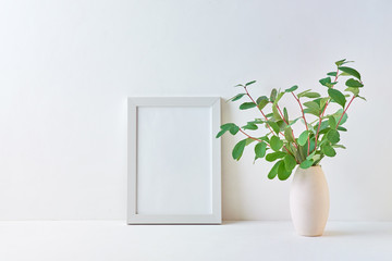 Mockup with a white frame and branches with green leaves in a vase on a light background