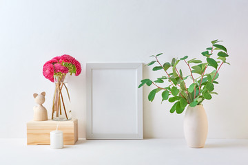 Home interior with decor elements. White frame, branches with green leaves in a vase, interior decoration