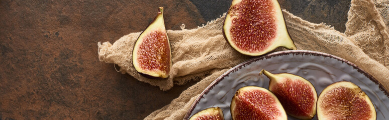 panoramic shot of cut ripe figs on white plate with rustic cloth on stone background