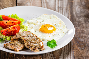 Grilled steaks with fried egg and vegetables on white plate