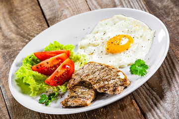 Grilled steaks with fried egg and vegetables on white plate