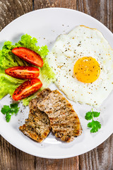 Grilled steaks with fried egg and vegetables on white plate