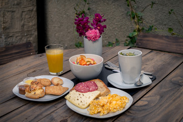 Breakfast consisting of a cup of coca tea, scrambled eggs, bread, slame, cheese, orange juice,...