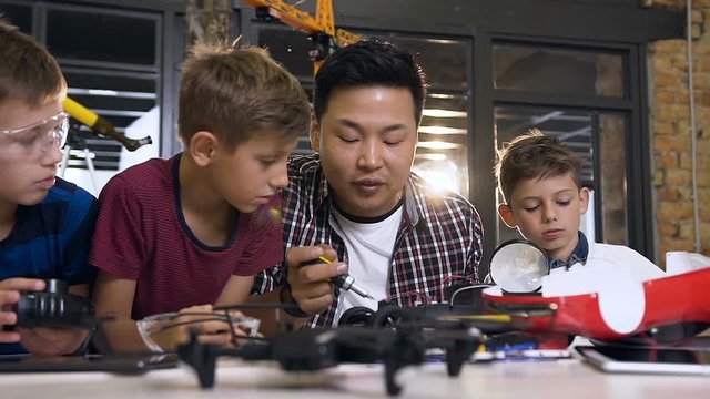 Asian electronic engineer with caucasian schoolchildren working in modern school lab and testing model electric car. Science and technology