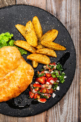 Fried pork chop, baked potatoes and vegetables on black stone plate