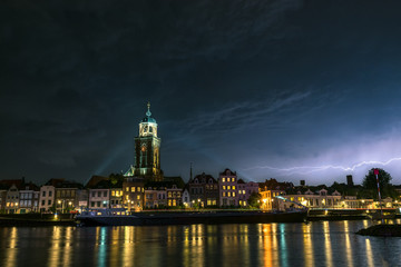 Fototapeta na wymiar Beautiful view of the city of Deventer, the Netherlands at night with colorful reflections in the water of the river IJssel. Lightning bolt above the skyline of the city.