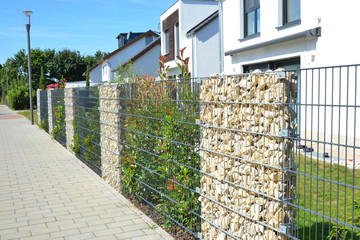 Moderner Sichtschutzzaun aus mit Naturstein gefüllten Gabionen und mit eingegrüntem verzinktem Stahlgitter vor einem neu gebauten Einfamilienhaus © Hermann
