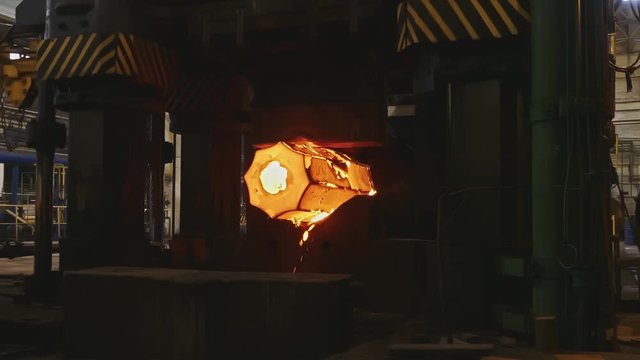 Molten metal blank. Billet forged in blacksmith the press. Machine Hammers a Glowing Steel Bar in the Foundry.  Сlose up large mechanical blacksmith hammer forges very hot iron bar in dark workshop..