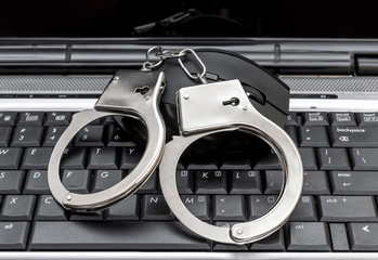 Computer mouse with handcuffs on the laptop keyboard. Close up. Cyber crime.