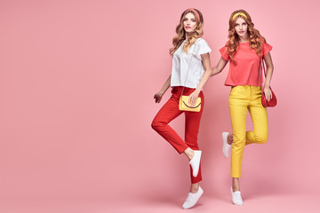 Two easy-going happy hipster Woman dance Fun in Stylish fashion colored red yellow pants. Beautiful excited Girl in summer Trendy outfit, sneakers jump laughing. Creative dancing fashionable concept