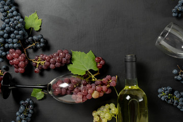 Bottle, two wine glasses, fresh grapes and leaves on black background. Flat lay, top view, copy...