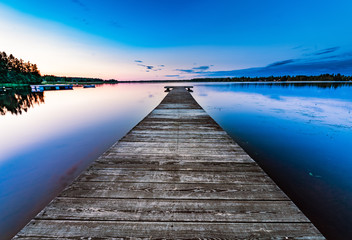 Very very long wooden bridge, almost to horizon, on the calm lake, summer sunset - blue rose skies reflected in still water. Northern Sweden