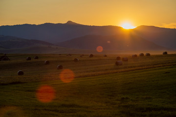 Obraz premium Sunset with haystacks and mountains in the background
