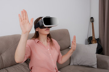 Woman using VR sitting on the couch with a sense of immersion in a virtual environment.