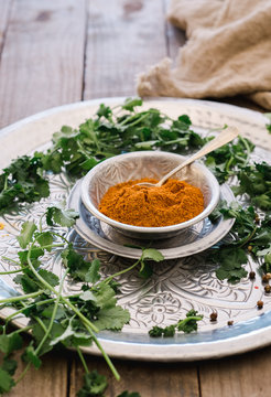 From above friable yellow turmeric in mug and greens on round silver plate on wooden table