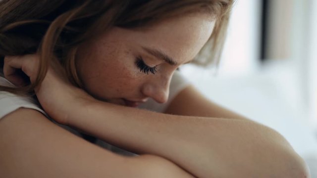 Sad young woman sitting in bedroom alone looking away feeling depressed mood and thinking about gloomy things unhappy expression