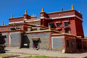 Unrecognizable monk sits on the doorstep of a large Buddhist monastery in Tibet.