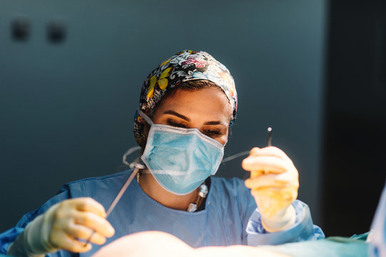 Plastic surgeon sewing up breast of female patient after inserting implants in operating room
