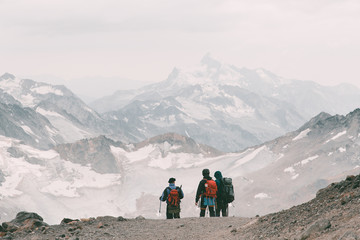 Extreme recreation and mountain tourism. A group of hikers down the mountain path over the horizon. In the background, large snow-capped mountains. Copy space.