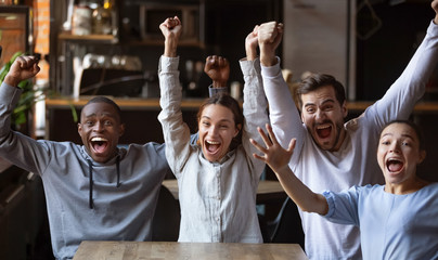 Excited diverse friends, football fans celebrating victory goal in cafe