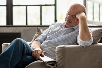Tired senior hispanic man with newspaper sleeping on couch, taking afternoon nap at the living room