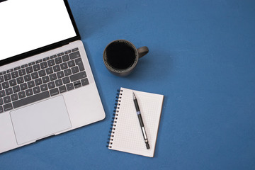 Top view workspace mockup, blank screen laptop, coffee mug, notepad and pencil on blue texture desk