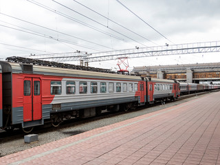 Obraz premium The train at the railway station on a cloudy day. Electric train, wagons, railway platform.