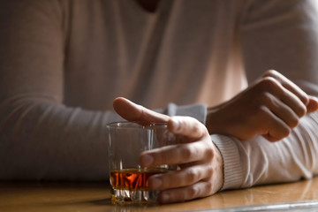 Close up man holding glass with alcohol in hand, drinking alone - obrazy, fototapety, plakaty