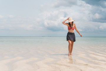 Fototapeta na wymiar NUNGWI, Zanzibar, Tanzania: woman wearing a sun hat walking on the beach with low tide. 