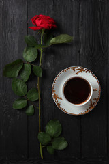 Red rose and a big cup with coffee on a black background. Morning drink concept.Bouquet of flowers.