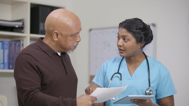 Nurse w/ stethoscope explains info on tablet and printout, camera move left