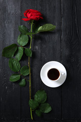 Red rose and cup with coffee on a black background. Morning drink concept.Bouquet of flowers.