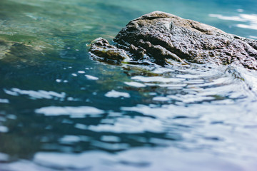 Stones in the clear water of the lake. Covered with moss and algae. Calm expanse of water with shallow waves.