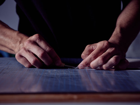 Faceless man working in bookmaking studio and measuring cover for book using pencil and ruler