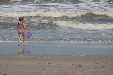 Little girl running with bucket to ocean