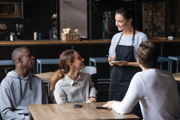Diverse friends making order in cafe, smiling waitress serving customers