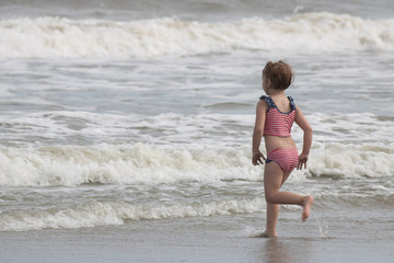 Little girl running toward ocean waves on the beach