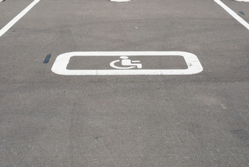 White disabled sign on a empty parking lot. Black tarmac texture with road marking 
