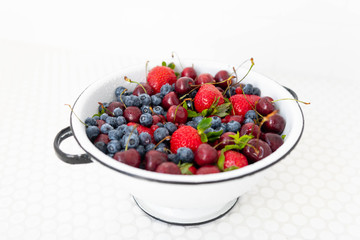 Colander Filled with Various Berries in White Tile Sink