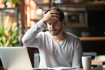 Upset man working in cafe, suffering from headache, touching forehead